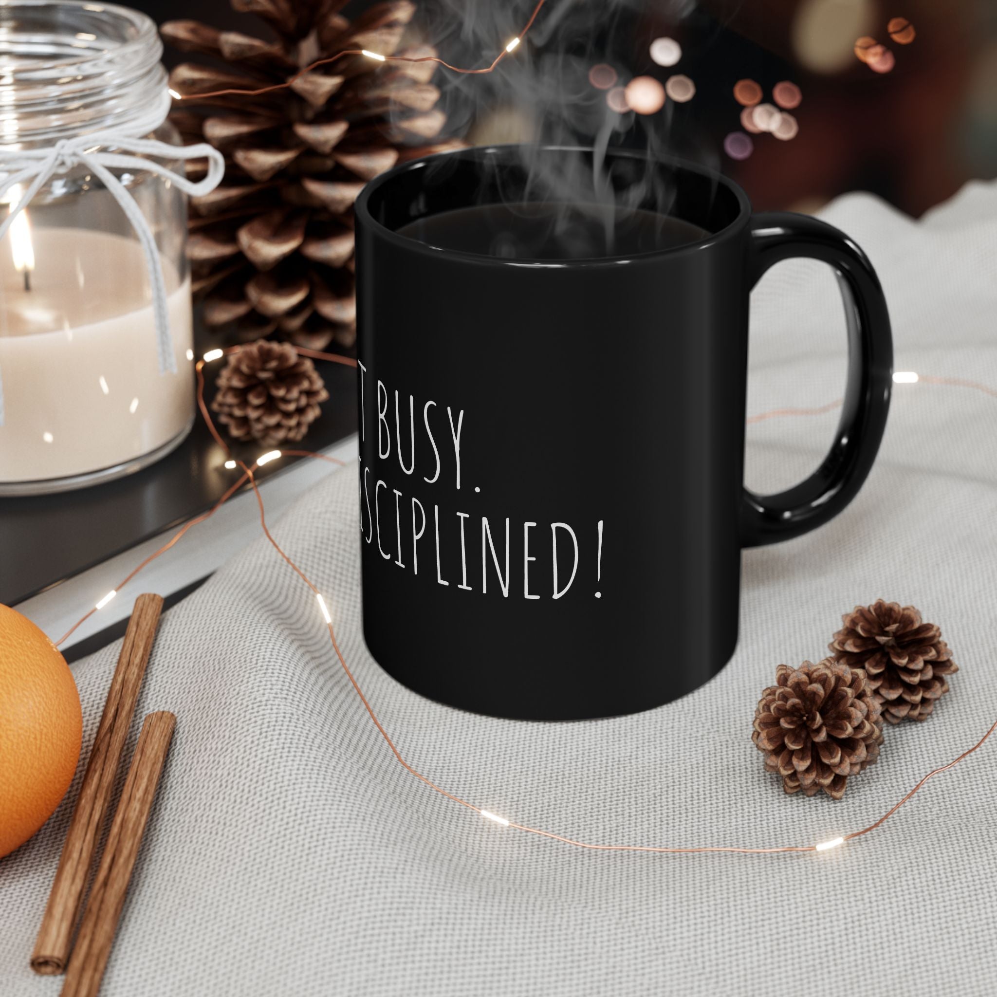Black mug with ' busy. Disciplined!' text, surrounded by decorative items on a table.